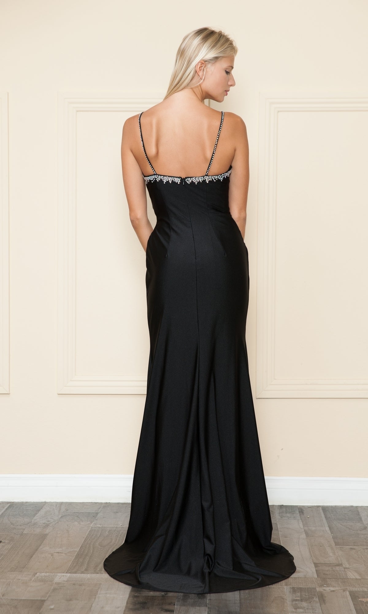 Woman models the Faux-Wrap Long Sweetheart Prom Dress (Poly USA 9134), a black evening gown with thin straps and rhinestone accents, standing with her back to the camera against a neutral indoor background.